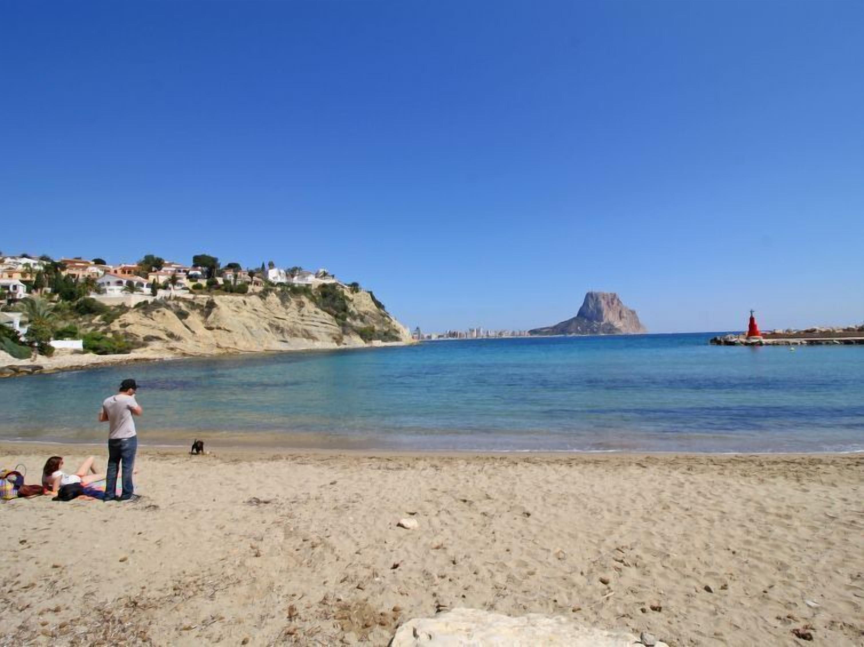 A beach with people relaxing, a rocky coastline, and a lighthouse in the distance.