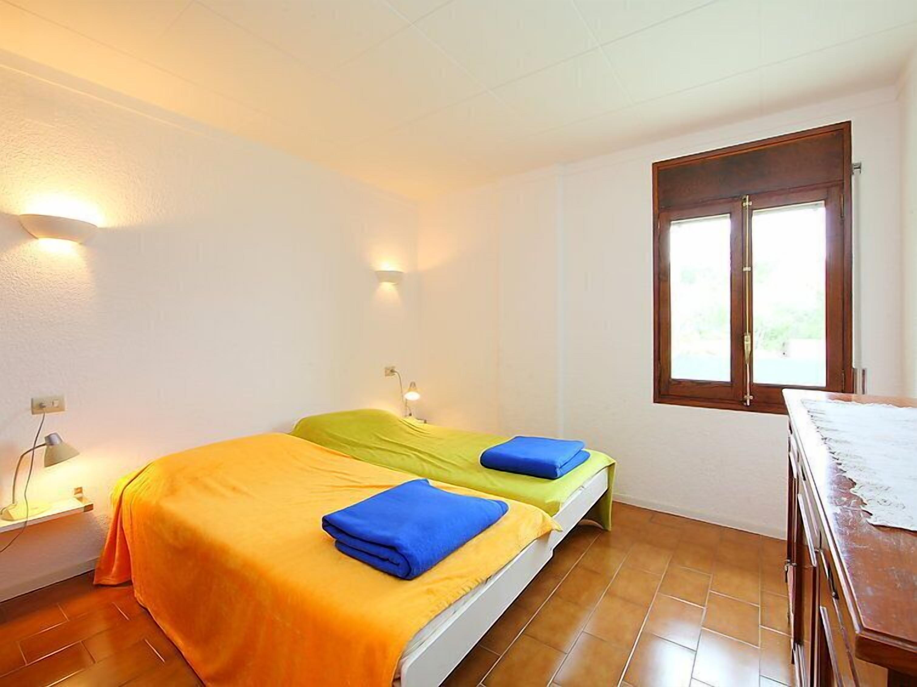 A room with two beds, each with a different colored bedspread, a desk, and a window with a view.
