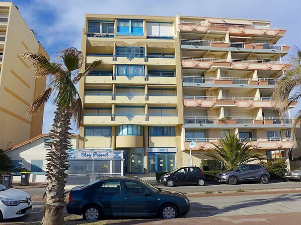 Un hotel de varios pisos con balcones, un restaurante visible llamado "Chez Pierre" y coches estacionados.