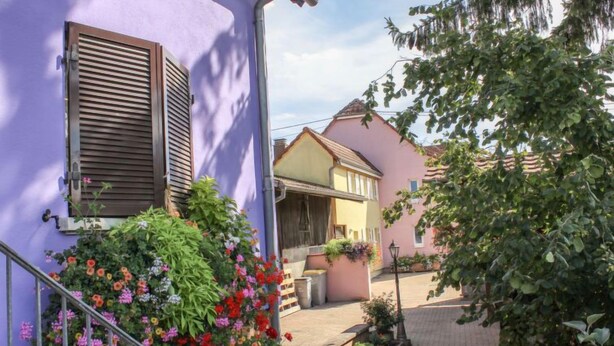 Eine schmale Straße mit Häusern an beiden Seiten, mit Balkonen und Blumenkästen sowie blauem Himmel.