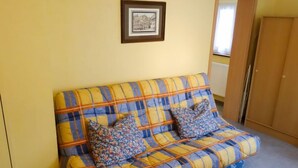 Eine gelbe Wand mit einem gerahmten Bild, ein kariertes Sofa mit zwei blumigen Kissen und ein Holzschrank.