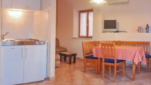A compact kitchen with white cabinets and a built-in stove. There is a dining area with a wooden table and chairs, covered with a checkered tablecloth. - Forlani by Interhome (Pula/Vodnjan)