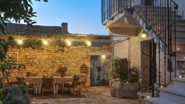 A stone courtyard with a table and chairs, surrounded by potted plants and string lights. - Forlani by Interhome (Pula/Vodnjan)