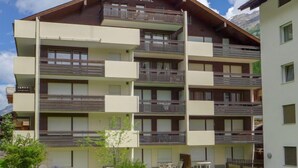 Un hotel de varios pisos con balcones, un cartel que dice 'IMPERIAL' y un paisaje montañoso de fondo.