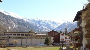 Un complejo turístico de montaña con edificios de estilo chalete, un patio vallado y montañas nevadas al fondo.