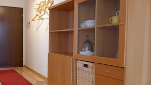 Una habitación con un armario de madera que contiene vajilla y una taza amarilla, una alfombra roja y una puerta de madera.