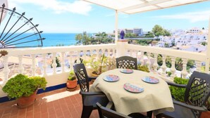 Un balcon avec vue sur la mer, une balustrade blanche et une table avec des chaises.