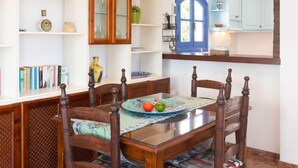 Un coin repas avec une table en bois, des chaises et une table avec un plateau en verre. On y trouve des étagères ornées d’objets décoratifs et un miroir au-dessus de la table.