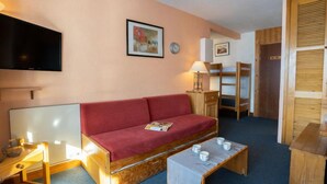 A cozy room with a red sofa, a flat-screen TV, a wooden coffee table, and a bunk bed. - Le Curling B (Val Claret) by Interhome (Tignes)