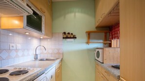 A compact kitchen with a microwave, stove, sink, and wooden cabinets. - Le Curling B (Val Claret) by Interhome (Tignes)