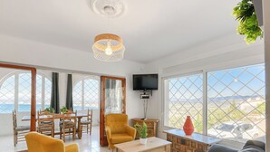 Ein geräumiges Wohnzimmer mit einem Holzesstisch, gelben Sesseln, einem grauen Sofa und einem an der Wand montierten Fernseher.