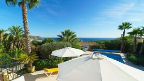 A pool area with a view of the sea, surrounded by palm trees and a white umbrella. - Las Boyas by Interhome (Moraira)
