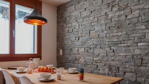 Ein Essbereich mit Holztisch, weißen Stühlen und einer Steinwand.