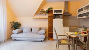 En kompakt opholdsstue med sofa, spisebord, tekøkken og trappe med hylder.