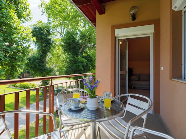 Ein Balkon mit Tisch, Stühlen, einer Topfpflanze und einem Glas Saft.