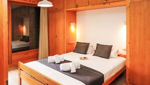 Un letto con struttura in legno, copriletto bianco e nero, due cuscini e asciugamani piegati con cura.