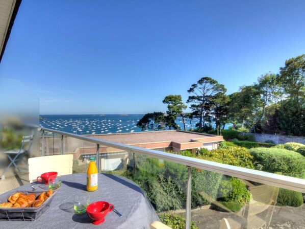 Un balcone con tavolo apparecchiato per la colazione, vista su un porto turistico con barche e un paesaggio costiero.