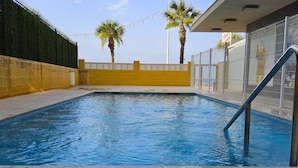 A rectangular swimming pool with a tiled edge, surrounded by a low yellow wall and a metal fence. - Tor Serena by Interhome (Benidorm)