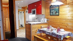Interior de madera con cocina que incluye armarios rojos, una isla central con pileta y una mesa de comedor servida con platos y vasos.
