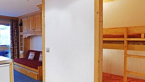 Habitación pequeña con literas, un sofá compacto y una kitchenette.
