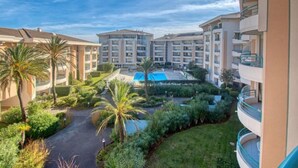 A multi-story hotel with a swimming pool surrounded by greenery and palm trees. - Le Cesarée by Interhome (Fréjus)