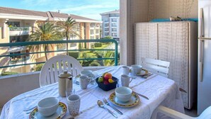 A balcony with a table set for breakfast, including plates, cups, and a fruit bowl. - Le Cesarée by Interhome (Fréjus)
