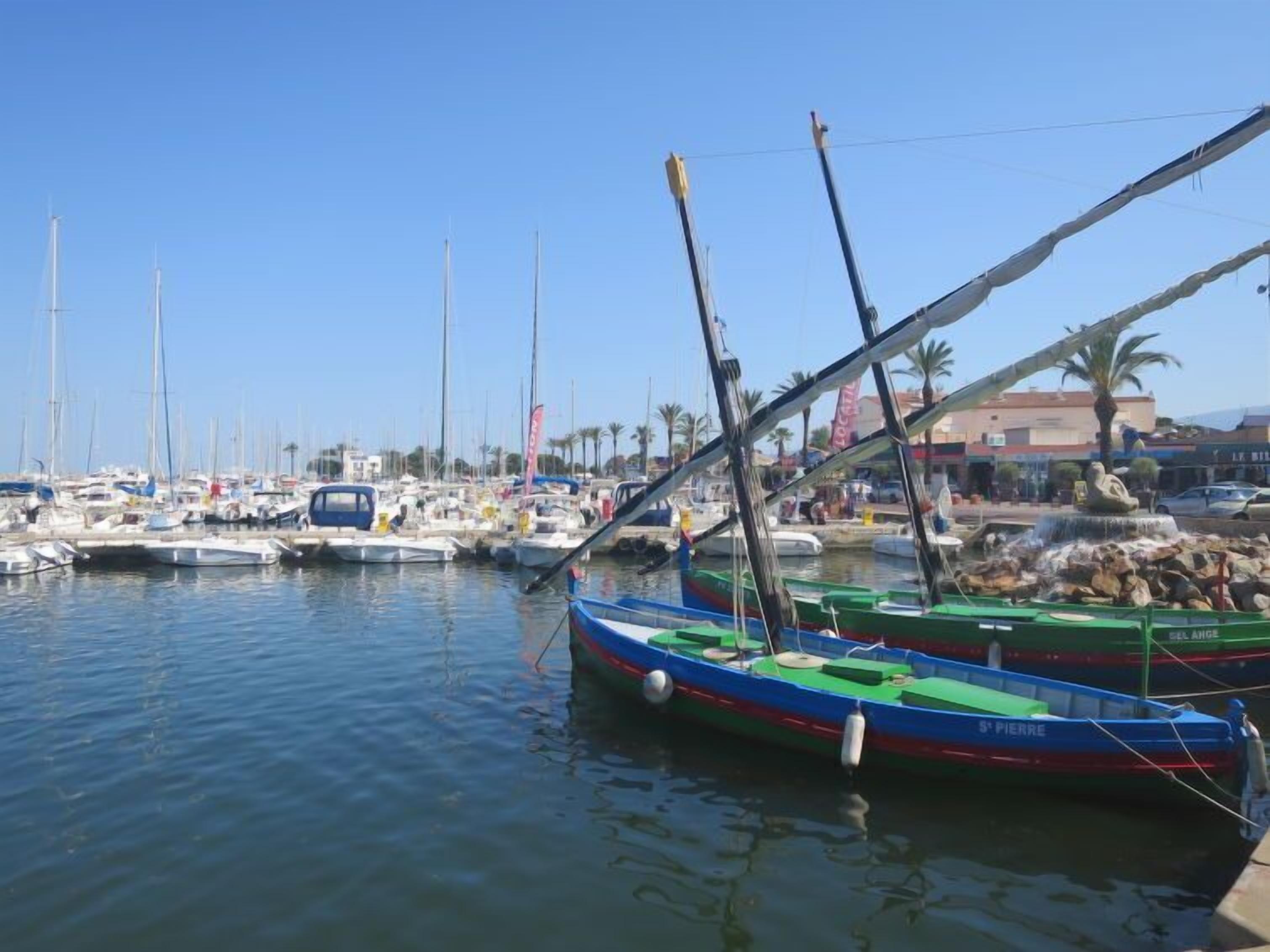 Een jachthaven met verschillende boten afgemeerd, een fontein en een helderblauwe lucht.