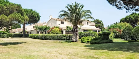 A large, two-story building with a tiled roof, surrounded by well-maintained lawns and various trees.