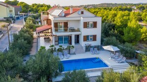 Ein modernes, zweistöckiges Haus mit Swimmingpool und Liegestühlen.