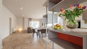 Eine moderne Wohnung mit Essbereich, einer Küche mit Obstschale und einem Wohnbereich mit Sofa.