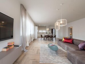 A modern living room with a flat-screen TV, a sofa, a coffee table, and a dining area in the background.