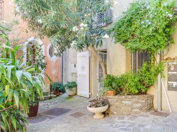A narrow courtyard with a stone floor, potted plants, and a door leading to a building.