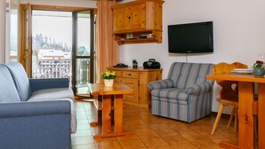 A cozy living room with a sofa, a striped armchair, a wooden dining table, and a television mounted on the wall. - Residenza Chesa Margun 57-1 by Interhome (Silvaplana-Surlej)