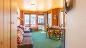 A cozy room with a wooden ceiling, a green carpet, a sofa with striped pillows, and a dining area with wooden chairs and a table. - Les Tufs (Val Claret) by Interhome (Tignes)