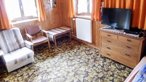 A cabin interior with a sofa, a small table, a TV on a dresser, and a patterned carpet.