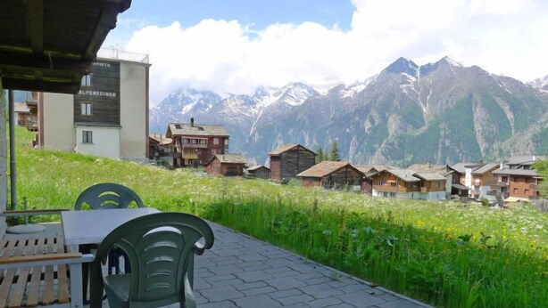 A terrace with a table and chairs overlooking a village with traditional houses and a mountain backdrop.