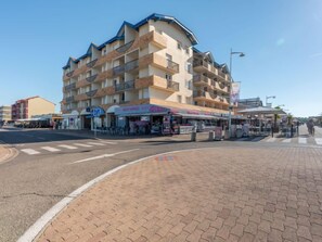 Hotel de varios pisos con balcones, una calle en la parte delantera y mesas al aire libre para cafés.
