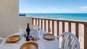 Ein Tisch für zwei mit einer Weinflasche, Gläsern und Tellern auf einem Balkon mit Blick auf den Strand.