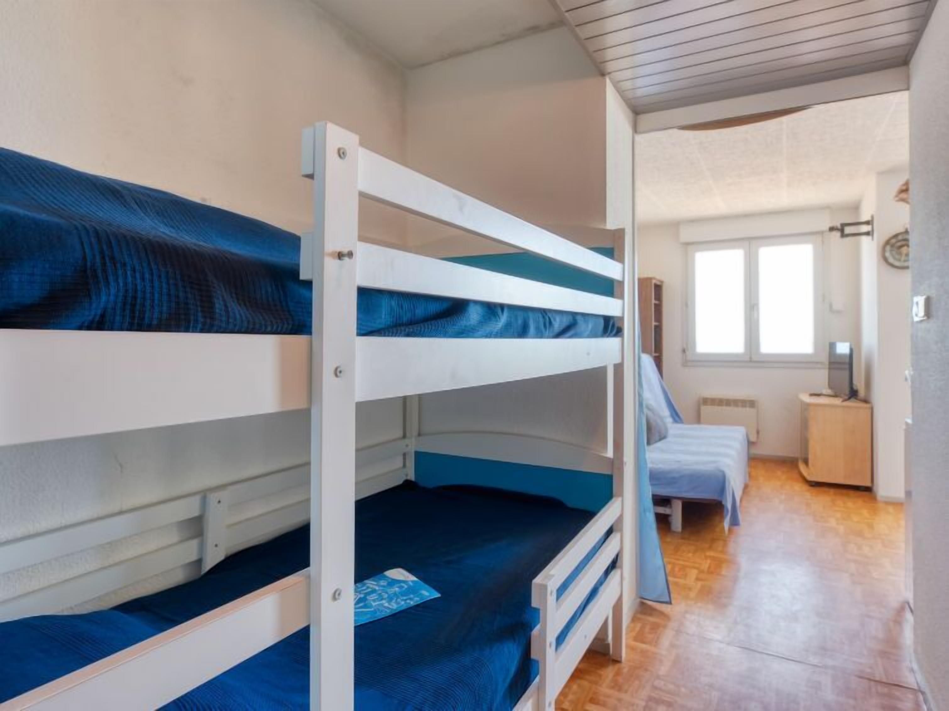 Ein Zimmer mit Etagenbetten, einem kleinen Schreibtisch, einem Stuhl und einem Fenster.