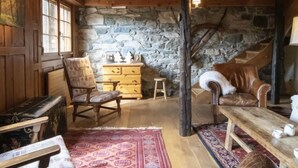 A rustic room with wooden beams, a stone wall, a wooden dresser, a chair, a sofa, and a staircase. - La Pive by Interhome (Verbier)