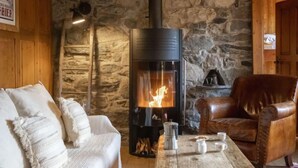 A cozy room with a stone wall, a fireplace, a sofa, a leather armchair, and a coffee table with cups and a pot. - La Pive by Interhome (Verbier)
