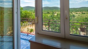 Quarto com varanda e vista para uma paisagem verde com colinas.