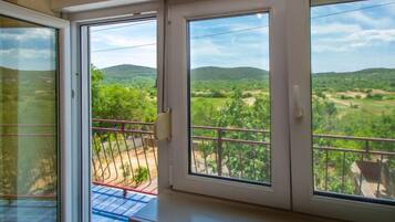 A room with a balcony overlooking a green landscape with hills.