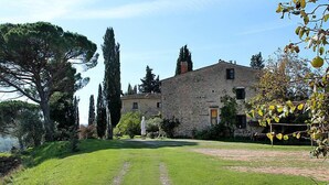 Un bâtiment en pierre avec une pelouse verdoyante et un chemin menant à l’entrée.