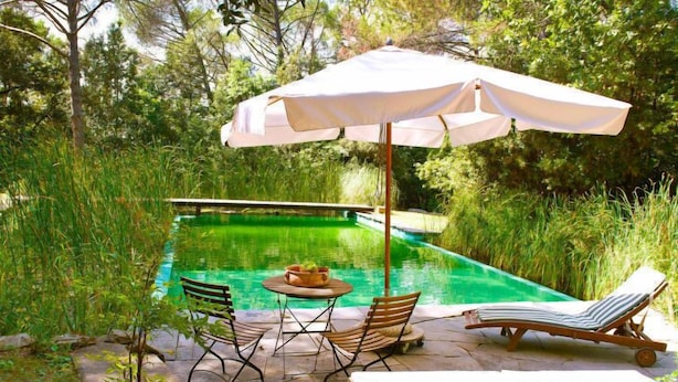 Un espace piscine comprenant une table et des chaises, un fauteuil de relaxation et un parasol.