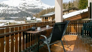 A balcony with a table, chairs, and a view of snow-covered mountains.