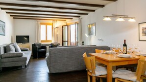 A modern living room with a sofa, a TV, and a dining area with a table set for a meal.