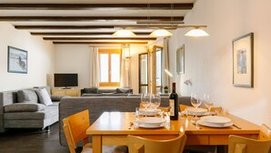 A dining area with a wooden table set for four, a sofa, and a television in the background.