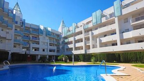 Ein modernes Hotel mit einem zentral gelegenen Schwimmbecken, umgeben von einem angelegten Garten und einem mehrstöckigen Gebäude mit Balkonen.