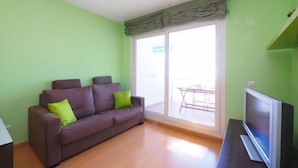 Ein Wohnzimmer mit einer Couch, einem Fernseher und einer Schiebetür zu einem Außenbereich.